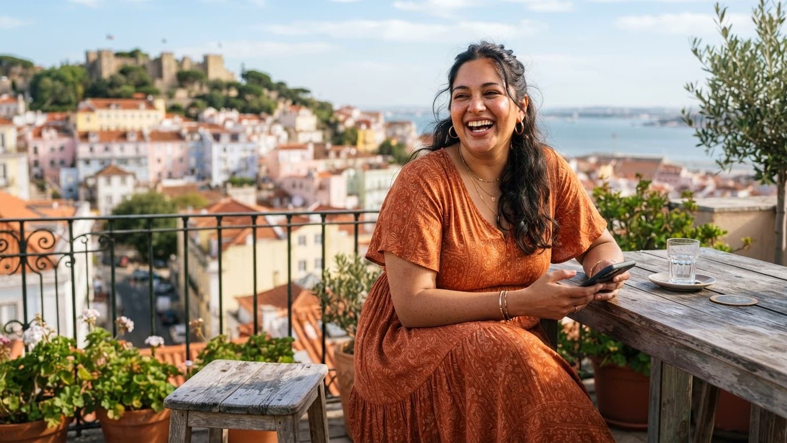 A woman laughing on a sunny rooftop terrace overlooking a coastal European city